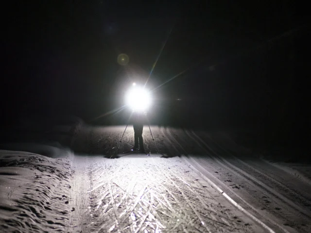 Silhouette d'un skieur nordique sur une piste de ski de fond enneigée de nuit avec une lampe frontale