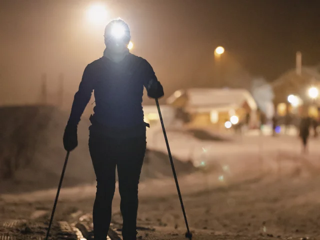 Une fondeuse sur une piste enneigée de nuit dans les traces de ski de fond classique avec une lampe frontale