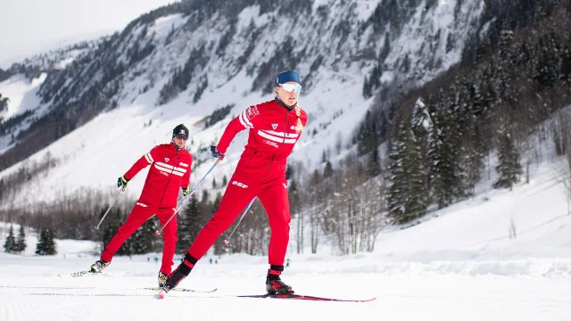Deux moniteurs nordiques de l'école de ski Français se suivent en skating sur une piste enneigée entourée d'un paysage montagnard enneigé et rempli de sapins