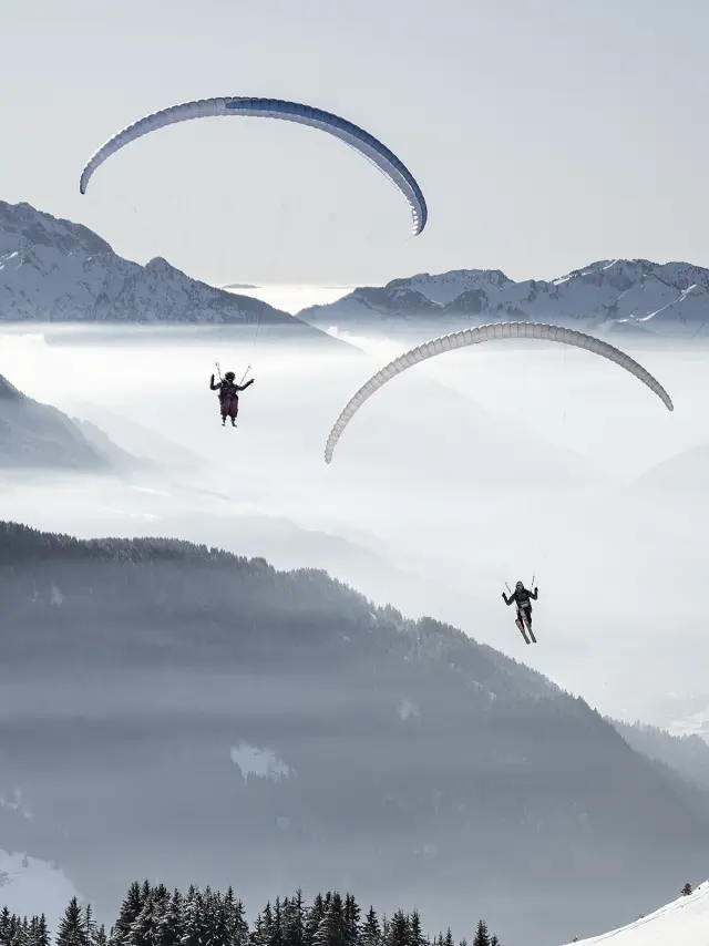 Deux parapentes volant sur les hauteurs du Grand-Bornand. L'ambiance est fraîche avec un léger voile nuageux.