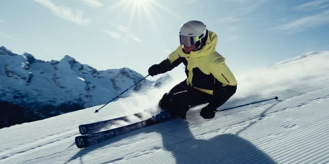 Skieur alpin en train de dévaler une pente dans un décors enneigé et un soleil éclatant