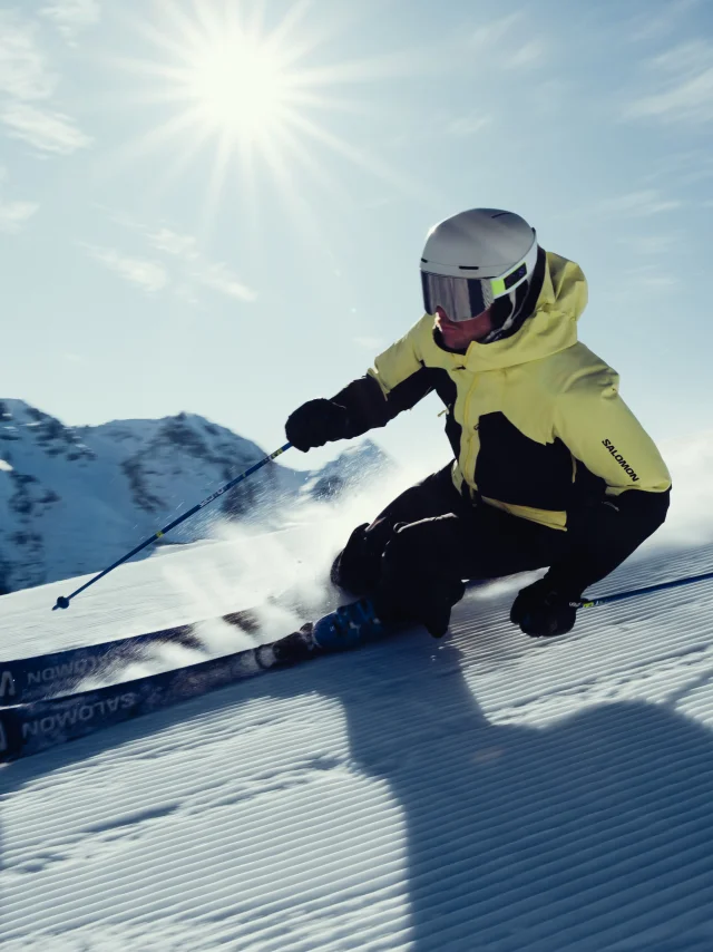Skieur alpin en train de dévaler une pente dans un décors enneigé et un soleil éclatant