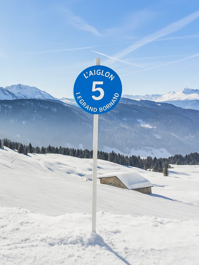 Panneau bleu indiquant la piste L'Aiglon numéro 5 à la station de ski Le Grand Bornand, avec un paysage enneigé et des montagnes en arrière-plan.