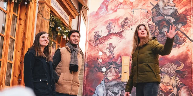 Deux personnes participent à une visite guidée du Village, et se trouvent devant une création du parcours de l'Art Vache, en plein hiver