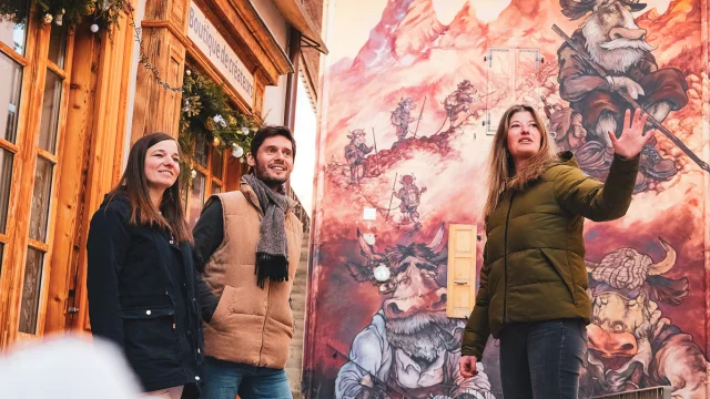 Deux personnes participent à une visite guidée du Village, et se trouvent devant une création du parcours de l'Art Vache, en plein hiver