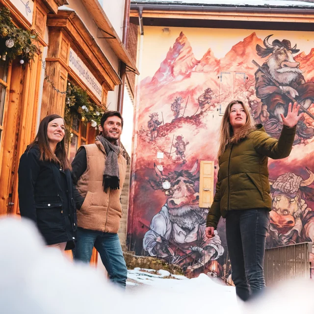 Deux personnes participent à une visite guidée du Village, et se trouvent devant une création du parcours de l'Art Vache, en plein hiver