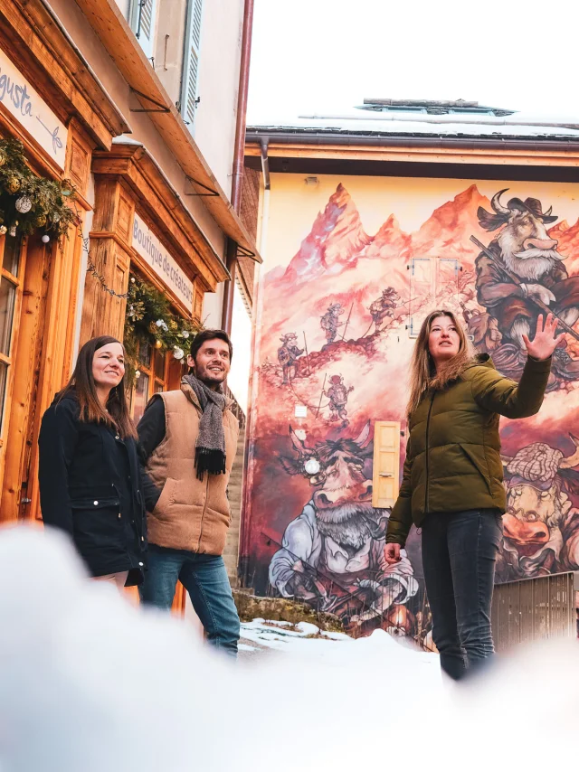 Deux personnes participent à une visite guidée du Village, et se trouvent devant une création du parcours de l'Art Vache, en plein hiver