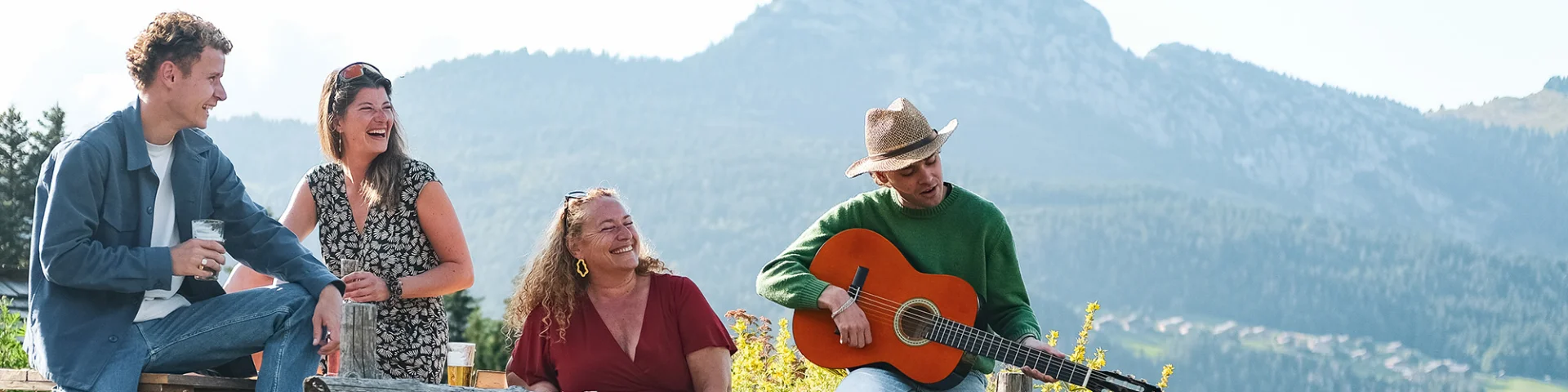 Moment de convivialité au restaurant les Frasses Jacquiers entre 4 personnes (2 femmes et 2 hommes, dont un jouant de la guitare). En toile de fond, le mont Bargy)
