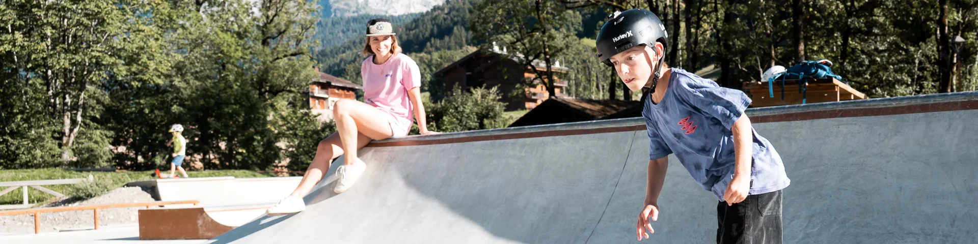 Un enfant fait du skate sur le nouveau skatepark du Grand-Bornand, sa mère, assise au bord, le regarde