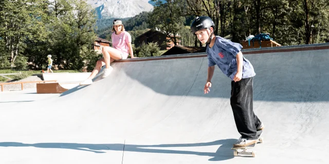 Un enfant fait du skate sur le nouveau skatepark du Grand-Bornand, sa mère, assise au bord, le regarde