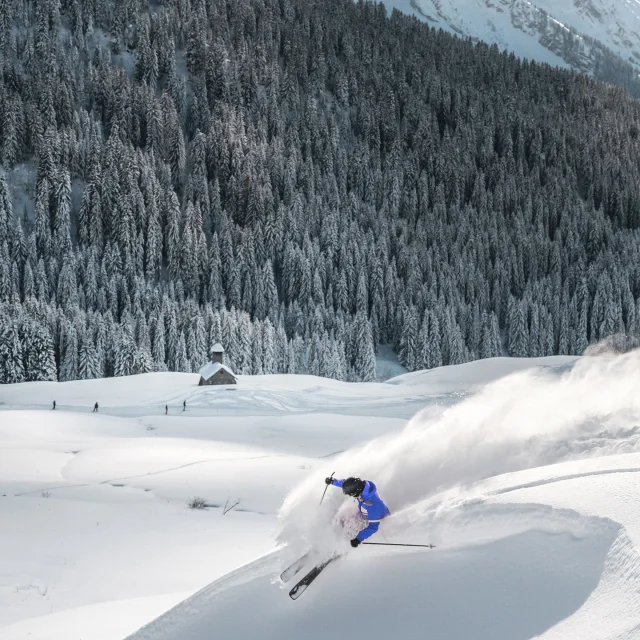 Skieur dévalant une piste et propulsant de la poudreuse