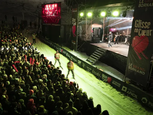 Scène de Glisse en Cœur en 2025 de nuit où des skieurs réalisent la course aux dons et passent devant la scène où M. Pokora performe avec une foule qui l'acclame
