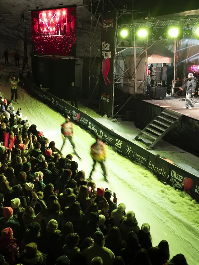 Scène de Glisse en Cœur en 2025 de nuit où des skieurs réalisent la course aux dons et passent devant la scène où M. Pokora performe avec une foule qui l'acclame