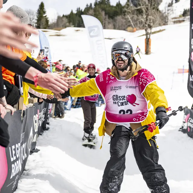 Un skieur participant à la course aux dons tape dans la main du public en passant à côté de la scène