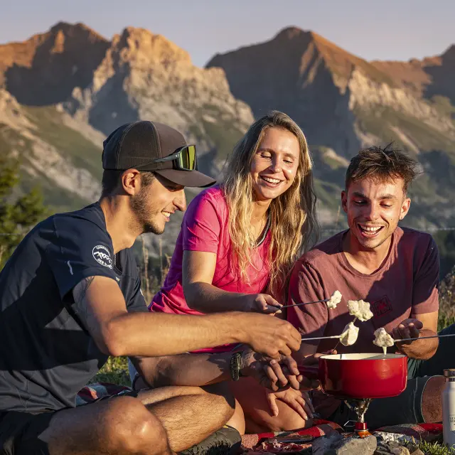 Un groupe d'amis profite d'une fondue au reblochon sur les hauteurs du Grand-Bornand, au coucher du soleil, en été