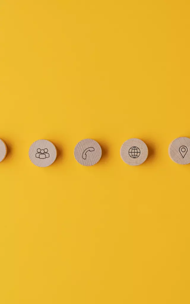 Five wooden cut circles with contact and information icons on them placed in a row over yellow background.