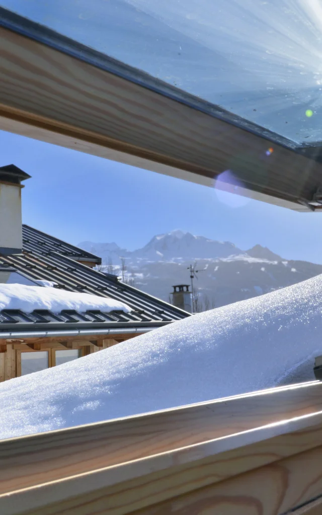 uitzicht vanuit een openslaand raam op een dak bedekt met sneeuw in een alpenhuisje
