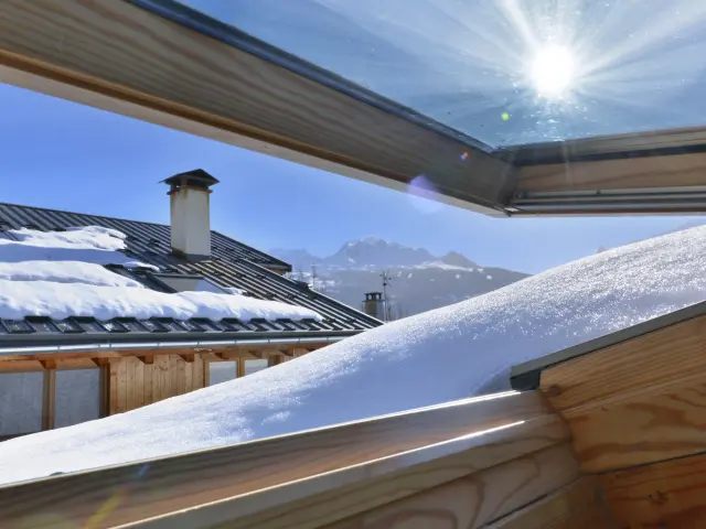 uitzicht vanuit een openslaand raam op een dak bedekt met sneeuw in een alpenhuisje