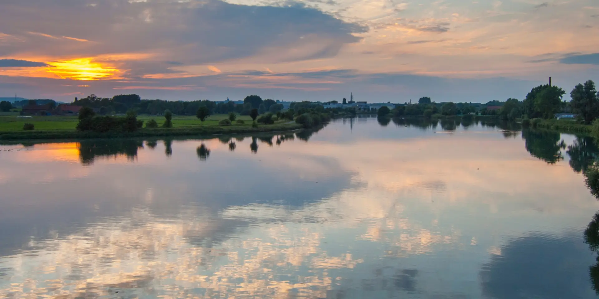 Coucher de soleil sur la confluence de la Deûle et de la Lys, reflets paisibles dans l’eau entourée de nature, au cœur de la métropole lilloise.