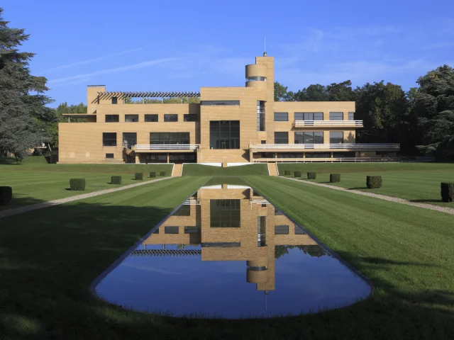 Vue symétrique de la Villa Cavrois à Croix, se reflétant dans le bassin au premier plan sous un ciel bleu dégagé.