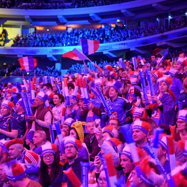 Tribunes remplies de supporters français brandissant drapeaux et bâtons gonflables bleu blanc rouge.