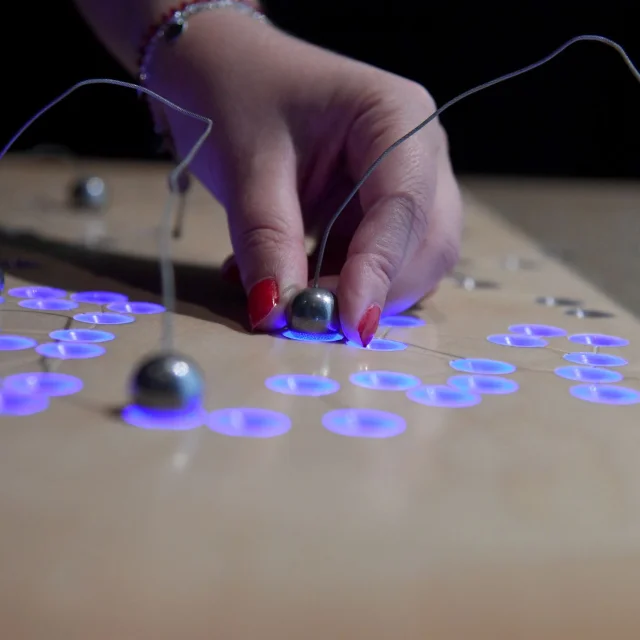 Main plaçant une bille métallique sur un plateau interactif lumineux au Forum départemental des sciences à Villeneuve-d’Ascq.
