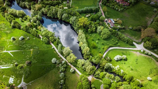 Vue aérienne du Lac du Héron entouré d’arbres et de sentiers, près de maisons rurales dans un paysage verdoyant.