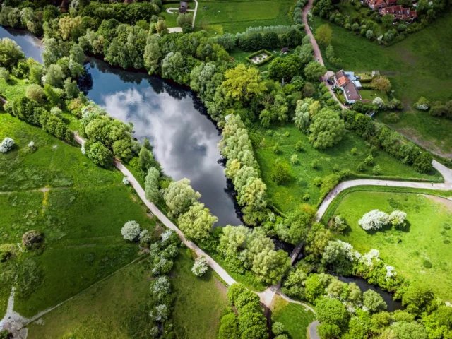 Vue aérienne du Lac du Héron entouré d’arbres et de sentiers, près de maisons rurales dans un paysage verdoyant.