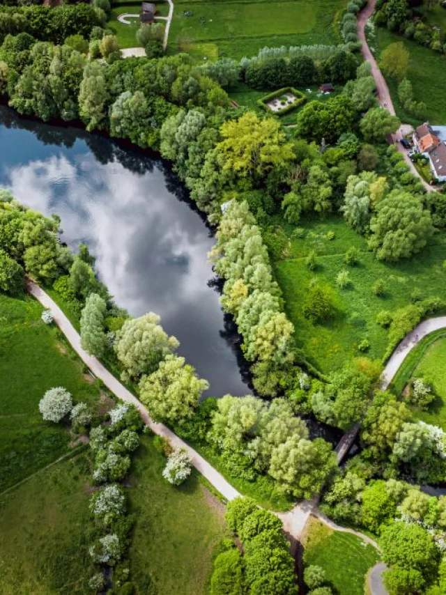 Vue aérienne du Lac du Héron entouré d’arbres et de sentiers, près de maisons rurales dans un paysage verdoyant.
