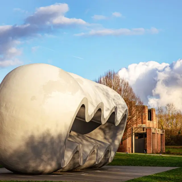 Grande sculpture blanche ondulée en plein air devant le musée LaM à Villeneuve-d’Ascq, sous un ciel bleu partiellement nuageux.