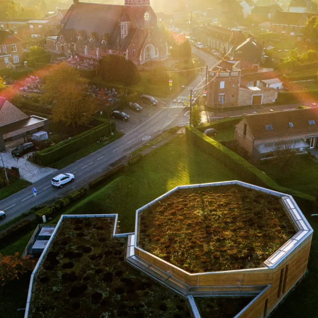 Vue aérienne au lever du soleil du Musée de la Bataille de Fromelles, au premier plan, avec son toit végétalisé, et l’église Saint-Jean-Baptiste en arrière-plan.