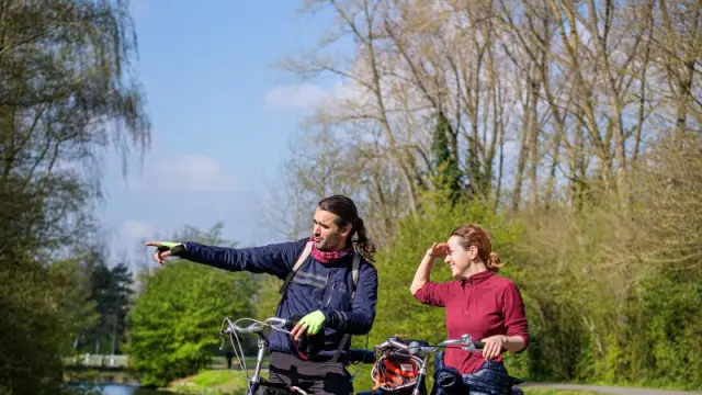 Un couple à vélo s’arrêtant près d’un canal, l’homme montrant un point au loin.