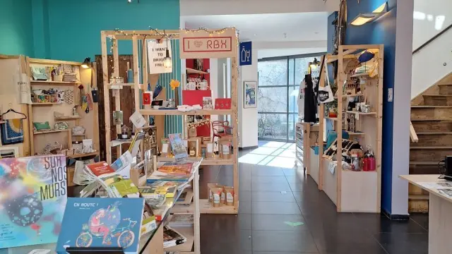 ue d’ensemble de la boutique de l’Office de Tourisme de Roubaix, mêlant ouvrages, produits artisanaux et décoration moderne sous plafond orné.