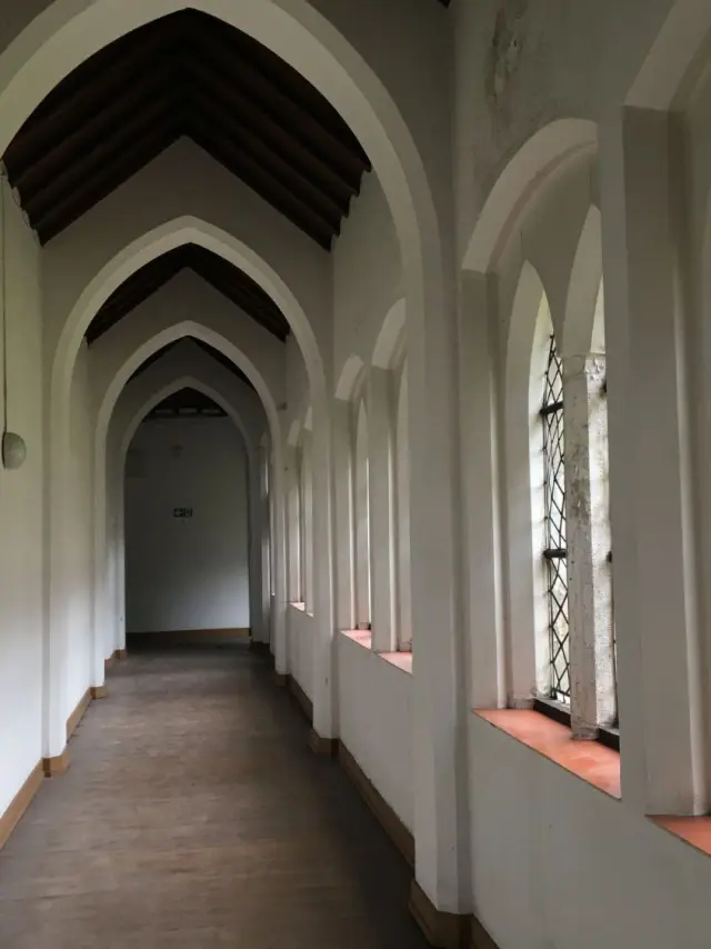Couloir du cloître du monastère des Clarisses à Roubaix, voûté en ogive et bordé de fenêtres à vitraux quadrillés.