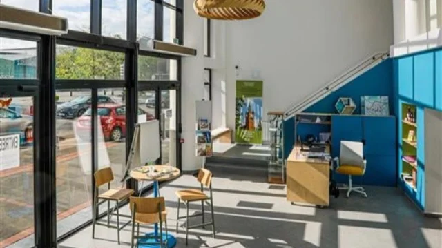 Hall lumineux de l’office de tourisme d’Armentières, avec mobilier d’accueil moderne, grande baie vitrée et suspensions design.