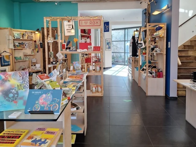 ue d’ensemble de la boutique de l’Office de Tourisme de Roubaix, mêlant ouvrages, produits artisanaux et décoration moderne sous plafond orné.