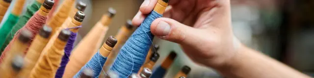 Main sélectionnant une bobine de fil bleu parmi des dizaines de bobines colorées dans un atelier textile.