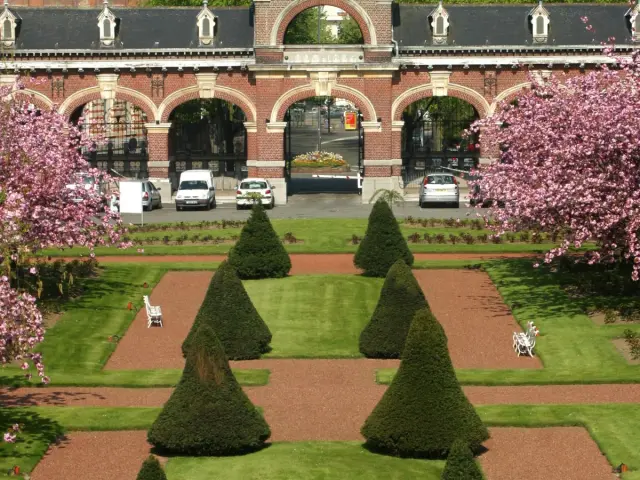 Allées symétriques bordées d’arbustes taillés et de cerisiers en fleurs dans le jardin intérieur de l’Hospice Barbieux à Roubaix.