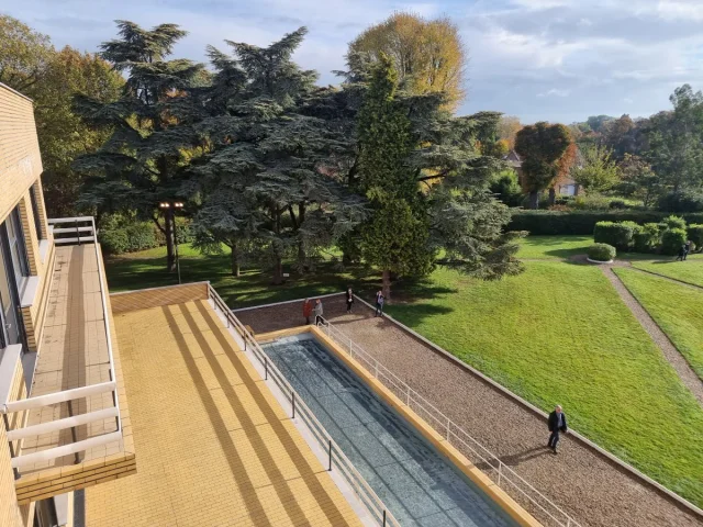 Vue plongeante sur le jardin et le bassin rectangulaire de la Villa Cavrois à Croix, bordés de grands arbres.