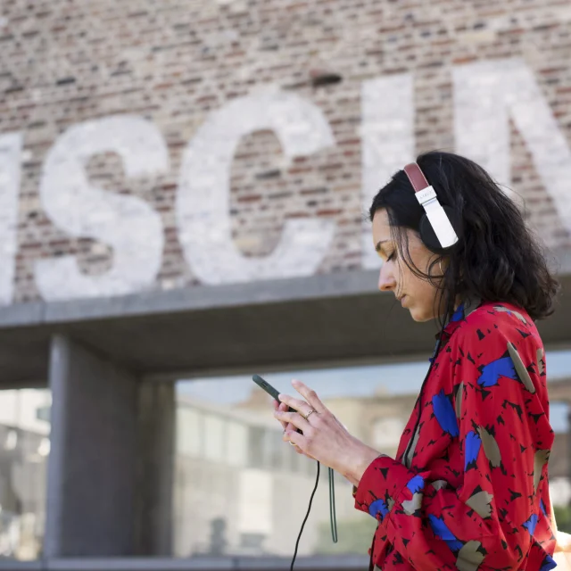 Femme avec un casque audio et un smartphone devant l'entrée en briques de La Piscine, musée d'art et d'industrie à Roubaix.