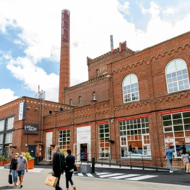 Façade en briques rouges de l’Usine à Roubaix, centre de marques installé dans une ancienne filature avec cheminée d’usine et passants en promenade.
