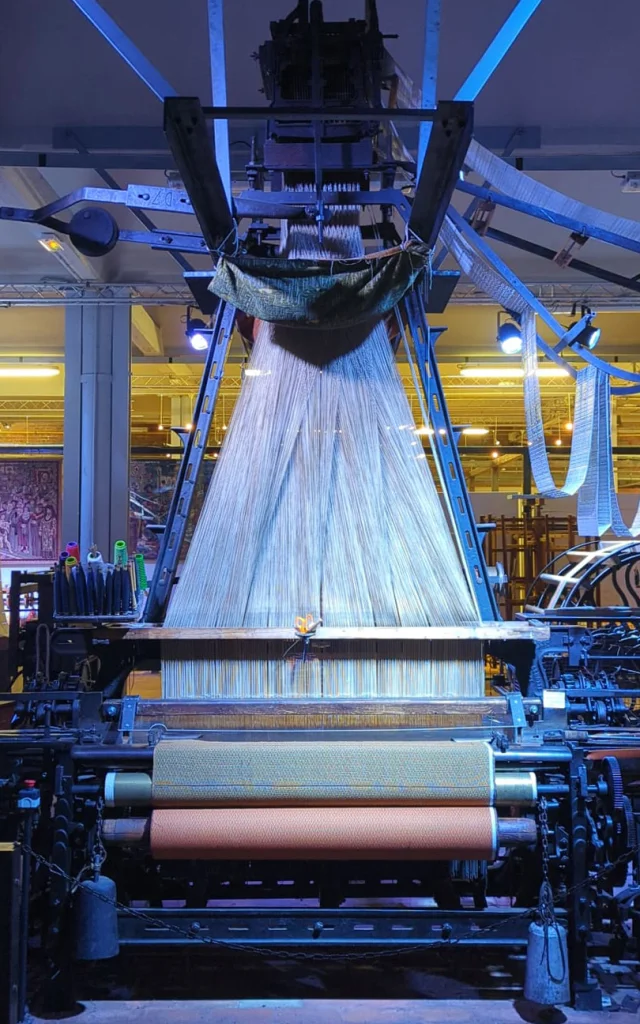 Métier à tisser mécanique exposé dans un musée textile à Roubaix, avec des fils tendus en cours de tissage.