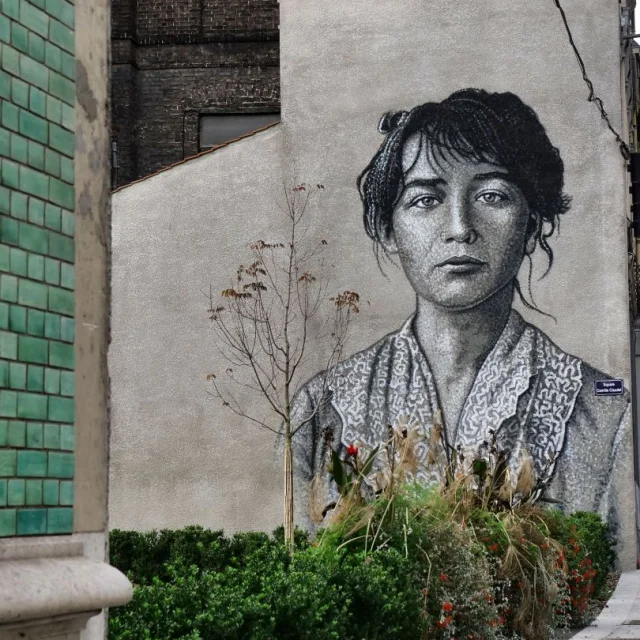 Fresque murale en noir et blanc de Camille Claudel réalisée par Jimmy C à Roubaix, près de la Maison verte, avec végétation en premier plan.
