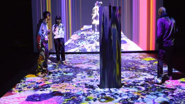 Trois personnes explorent une installation immersive aux projections colorées lors d'une exposition.