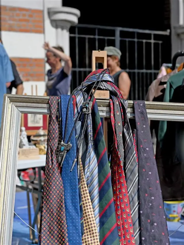 Stand de la Braderie de Lille avec cravates suspendues dans un cadre, vaisselle ancienne et ambiance conviviale entre chineurs.