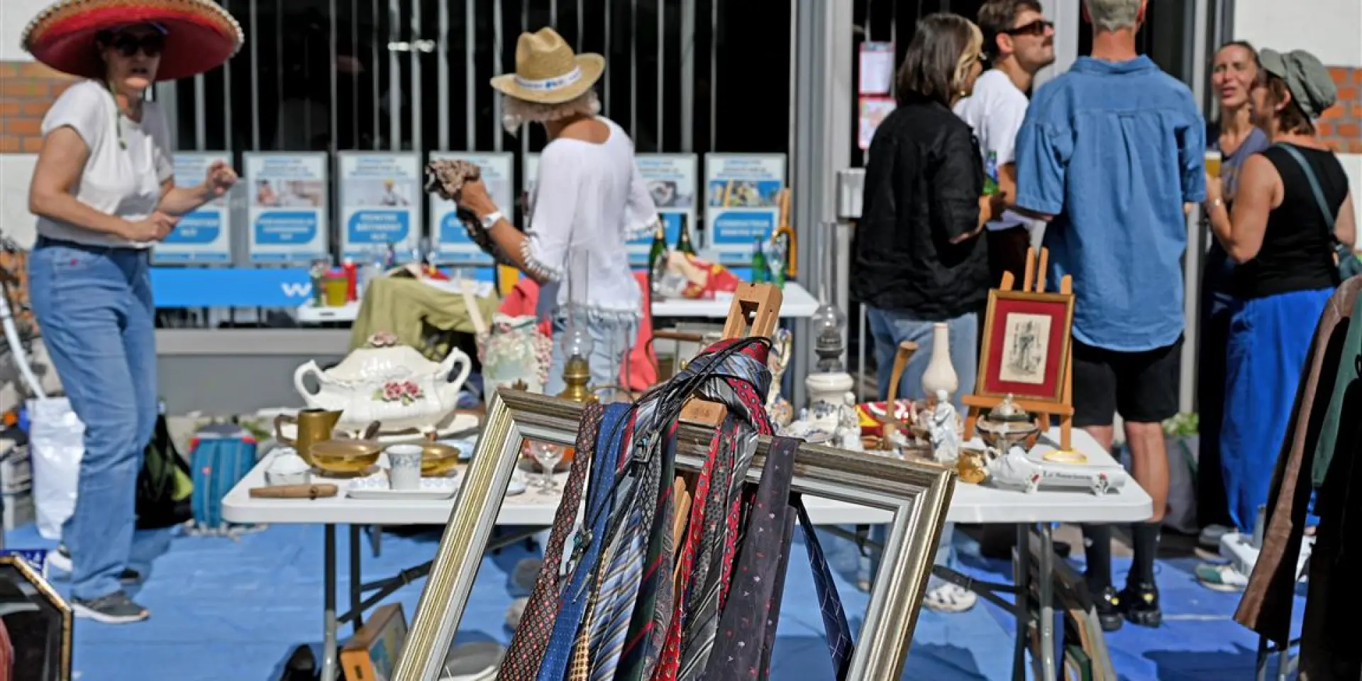 Stand de la Braderie de Lille avec cravates suspendues dans un cadre, vaisselle ancienne et ambiance conviviale entre chineurs.