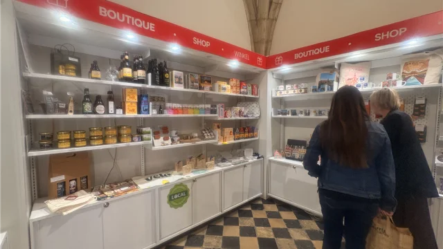 La photo montre l’intérieur d’une boutique touristique, avec des rayonnages garnis de produits locaux et souvenirs de Lille et de la Métropole : mugs, cartes postales, spécialités régionales, magnets, objets à l’effigie de la Braderie de Lille, etc. L’ambiance est lumineuse et accueillante.
