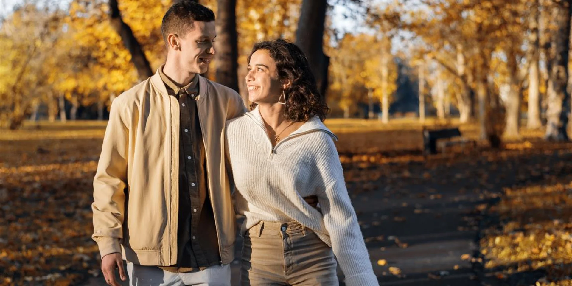 Een romantisch stel in een herfstpark. Wandelend over het pad, elkaar vasthoudend en naar elkaar kijkend. Herfstsfeer, vergeelde bomen en bladeren rondom
