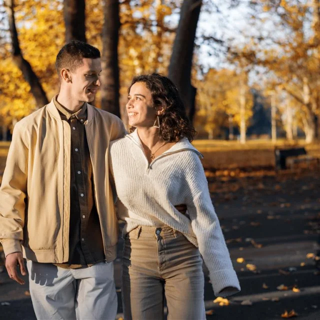 A romantic couple in an autumn park. Walking along the path holding and looking at each other. Autumn atmosphere, yellowed trees and leaves around