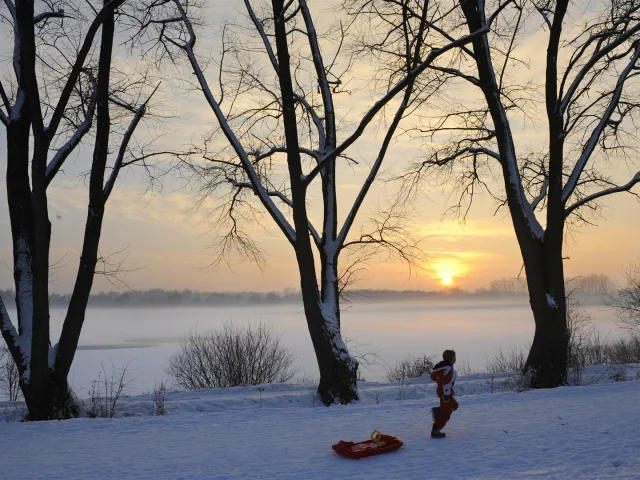 Enfant tirant une luge rouge sur la neige au lever du soleil près du lac du Héron.